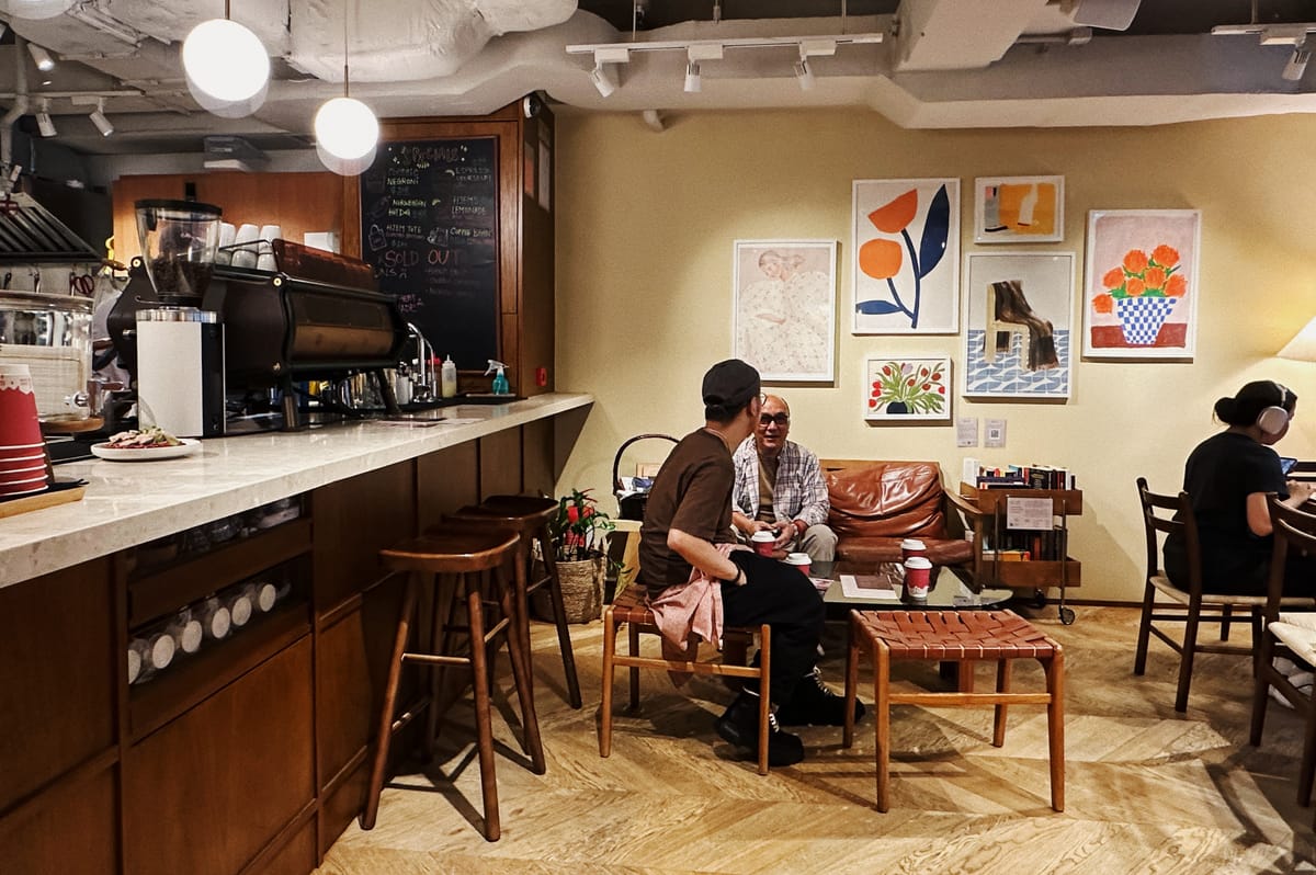 two man in a nordic cafe with wall art pieces, a woman with headphones is working